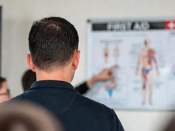 First aid trainer explaining anatomy on a wall chart to a group of learners during a training session